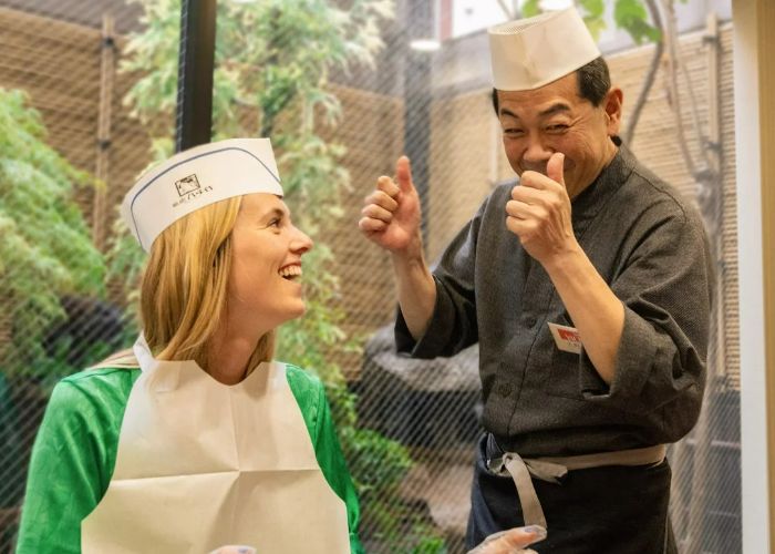 A private sushi-making class where the host is giving a thumbs up to the camera while smiling.